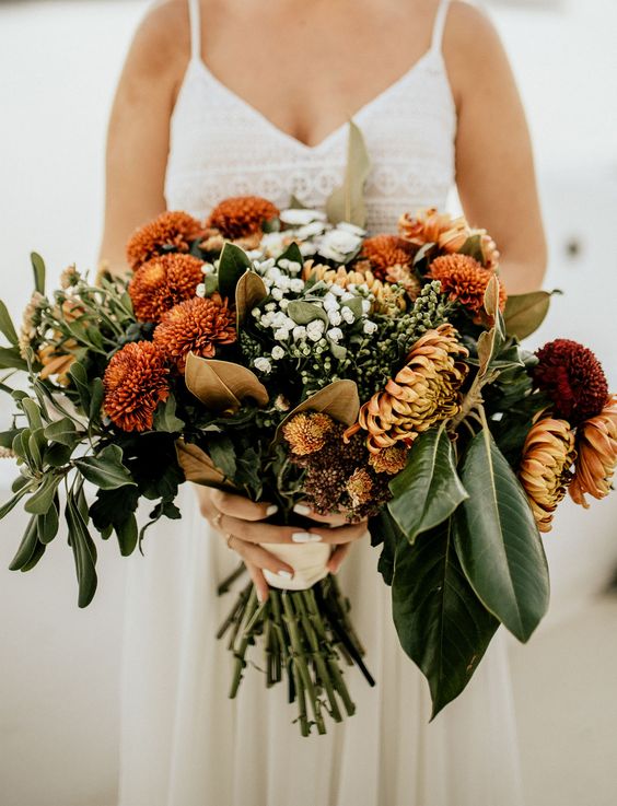 an earthy-tone fall wedding bouquet of orange, rust and white blooms, greenery and foliage is a stunning idea for the fall