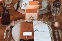 an exquisite wedding tablescape with rust napkins, menus and blooms, amber bottles and white porcelain