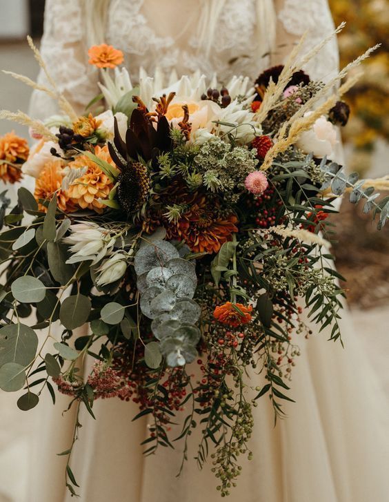 an incredibly lush fall wedding bouquet of orange, rust, pink, deep purple and yellow blooms, lots of various greenery, wheat and berries
