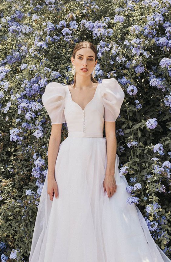 an ivory A-line wedding dress with a cutout neckline, a row of buttons, puff sleeves and a tulle skirt plus statement earrings