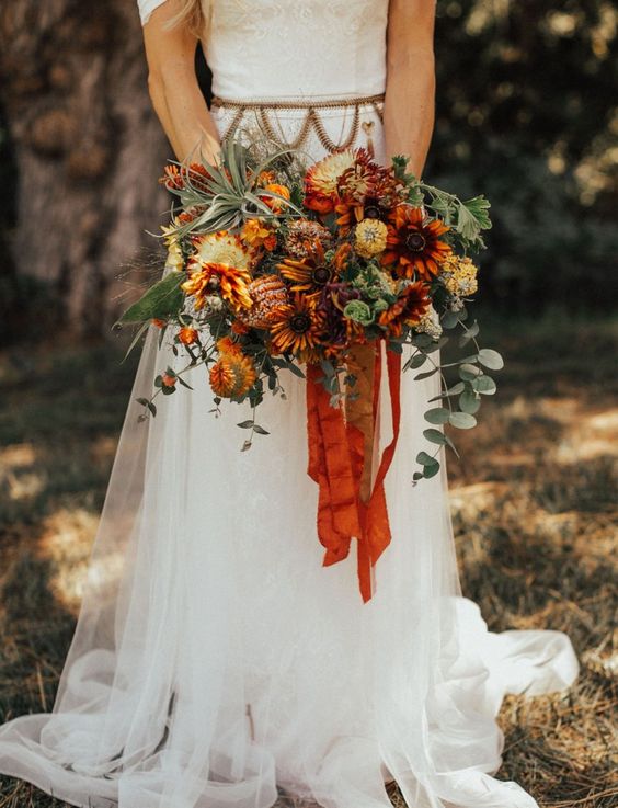 an out of the box fall wedding bouquet of orange, rust and burgundy blooms, greenery, berries and air plants plus orange ribbons is a stunning idea