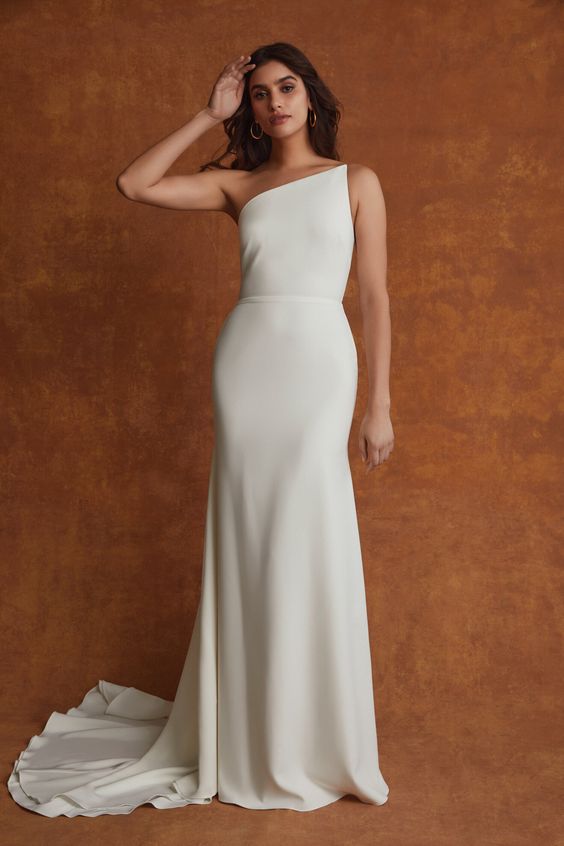 an ultra minimalist one shoulder semi fitting wedding dress with a sash and a train   you won't need anything else to make a statement