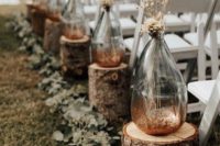 bottles with copper glitter and dried grasses, tree stumps and eucalyptus for an outdoor fall wedding aisle
