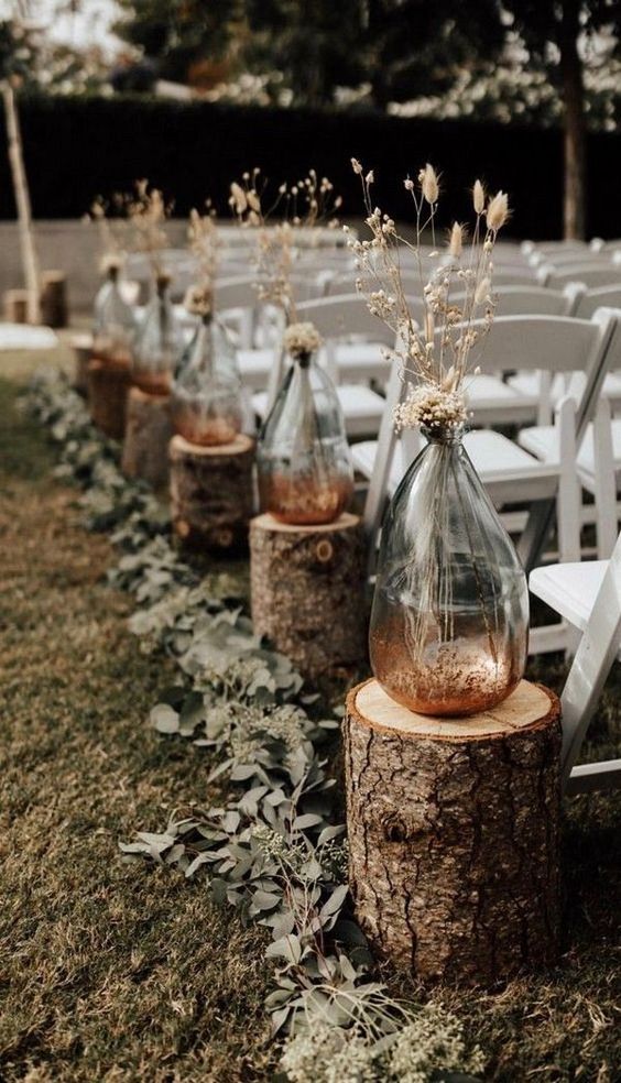 bottles with copper glitter and dried grasses, tree stumps and eucalyptus for an outdoor fall wedding aisle