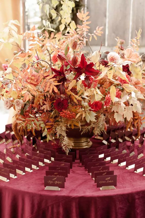 display burgundy escort cards around a gold vase with bright blooms, berries and white leaves for the fall