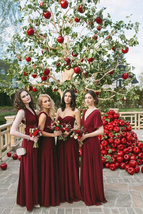 mismatching deep red bridesmaid maxi dresses and a stack of red apples for wedding decor