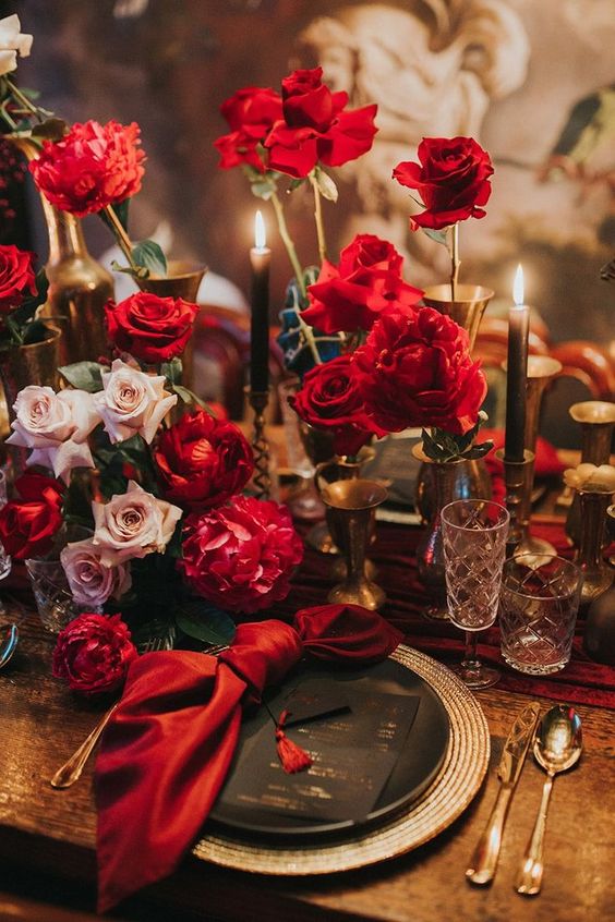 a beautiful Halloween wedding tablescape with plenty of red and blush roses, red napkins, gold touches and black plates
