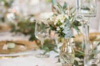 a beautiful neutral wedding tablescape with gilded chargers and cutlery, clear vases and glasses and tall and thin light green candles