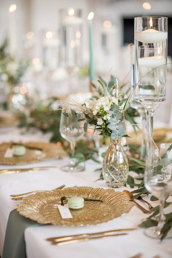a beautiful neutral wedding tablescape with gilded chargers and cutlery, clear vases and glasses and tall and thin light green candles