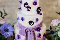 a beautiful ombre white to purple wedding cake decorated with gold leaf, with pansies and a purple ribbon bow is amazing