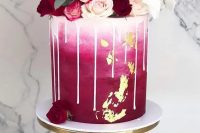 a beautiful wedding cake with ombre white to fuchsia decor, creamy drip, white, blush and burgundy blooms on top