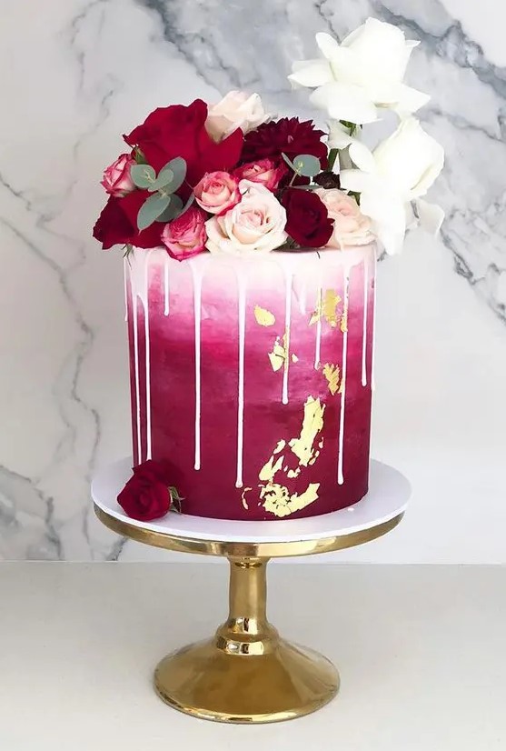 a beautiful wedding cake with ombre white to fuchsia decor, creamy drip, white, blush and burgundy blooms on top