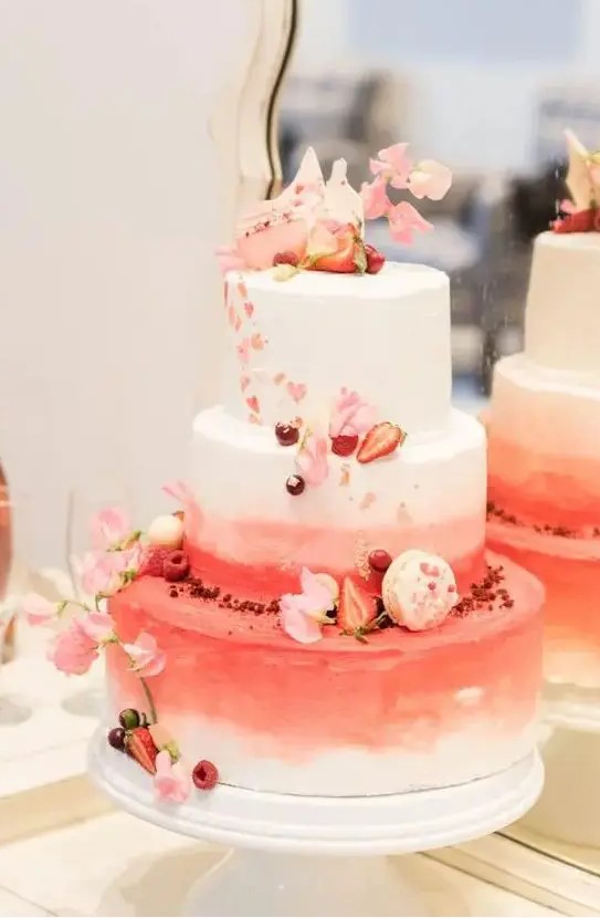 a beautiful white, pink and red wedding cake decorated with pink blooms, strawberries and macarons for a Valentine wedding