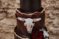 a black and burgundy wedding cake with a gold edge, a skull, blooms and skeleton toppers for Halloween