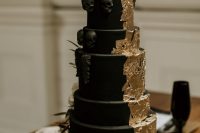 a black matte wedding cake with gold leaf, sugar skulls and a large gold skull ont op is very chic
