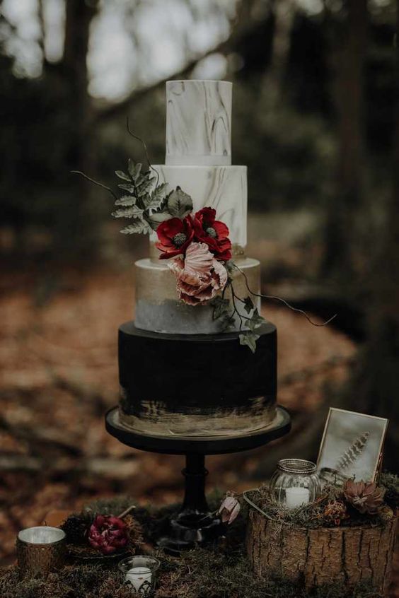 a black, white and gold wedding cake with marble tiers, gold leaf, sugar blooms and leaves plus branches for a Halloween wedding