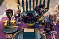 a breathtaking Halloween wedding table with a purple runner, deep purple and burgundy blooms, gold cutlery, placemats and candleholders