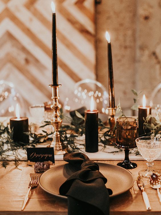 a chic Halloween wedding table with a greenery runner, black candles and napkins, black glasses and gold cutlery
