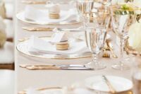 a classic gold and ivory wedding table setting with clear chargers, gold cutlery and gold-rimmed glasses plus white blooms