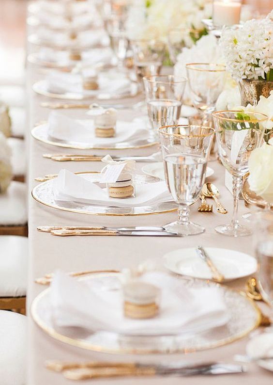 a classic gold and ivory wedding table setting with clear chargers, gold cutlery and gold-rimmed glasses plus white blooms