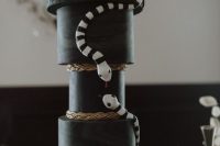 a creative All Hallows Eve black wedding cake with gold drip and black and white snakes is fabulous