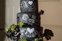 a creative chalkboard wedding cake with painted skulls, greenery, succulents and sugar skull toppers for a Halloween celebration