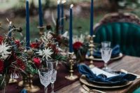 a dark romance Halloween wedding tablescape with teal napkins and candles, a burgundy runner and floral arrangements plus gold