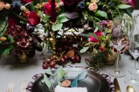 a decadent Halloween wedding tablescape with black plates and burgundy candles and napkins, lush and bold floral centerpieces