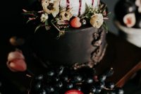 a decadent wedding cake with a black and a naked tier, berry drip, berries and fruits plus blooms on top