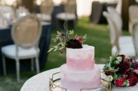 a delicate ombre pink buttercream wedding cake with a pink and a deep purple bloom and some greenery for a refined wedding