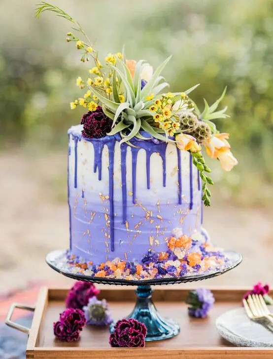 a gorgeous ombre violet wedding cake with violet drip, with bold florals and greenery on top and a bit of colored sugar is fun and cool