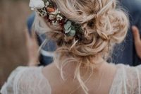 a messy and loose wedding low updo with waves and locks down and with a floral accent – neutral and blush blooms and greenery