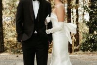 a modern sophisticated bridal look with a strapless plain wedding dress with a big bow on the back and matching long gloves plus pearl earrings