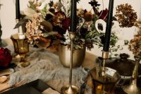 a moody Halloween wedding tablescape with a grey runner, black plates and candles, gold vases and candleholders