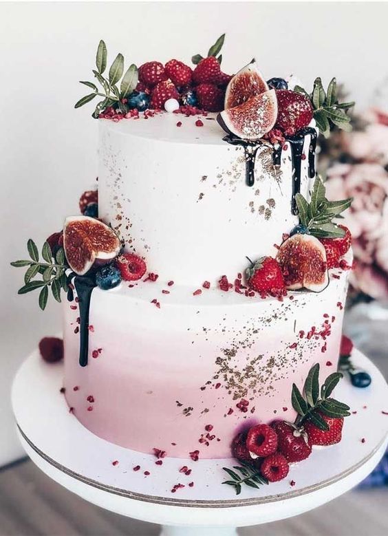 a mouth-watering ombre pink wedding cake with gold glitter, chocolate drip, fresh fruit, berries and greenery is amazing for summer