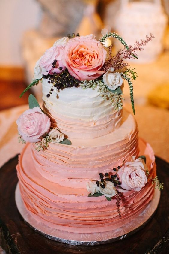 a pretty and lovely ombre pink ruffle buttercream wedding cake with white, pink and peachy blooms, privet berries and greenery