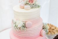 a pretty rustic wedding cake in ombre pink, with textural buttercream, pink and neutral macarons, white and pink blooms and a calligraphy topper