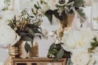 a pretty wedding centerpiece of vintage gold vases with white blooms and greenery and a mirror in a frame is a lovely decor idea