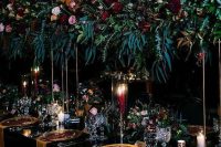 a refined Halloween wedding table setting with a black tablecloth, mustard napkins and chargers, lush floral and greenery arrangements