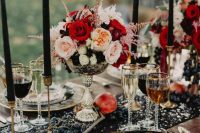 a refined Halloween wedding table with a gold sequin table runner, black candles and plates, bold floral arrangements and fruit on the table