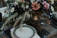 a refined Halloween wedding table with black marble chargers, black cutlery, a lush floral arrangement with greenery