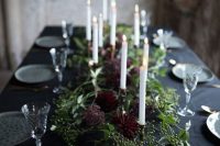 a refined Halloween wedding tablescape with a black tablecloth, printed plates, lush greenery and deep purple blooms and candles