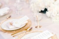 a refined white and gold wedding tablescape with a gold charger, gold cutlery and white blooms, pillar candles in glasses is a lovely idea