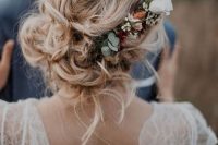 a relaxed and messy low bun with waves down and a neutral flower accent with greenery for a fall boho wedding