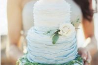 a ruffled ombre wedding cake from white to blue, with greenery and a neutral flower for a beach or coastal wedding