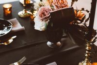 a soft gothic Halloween tablescape with a black tablecloth, plates and candles, blush blooms and napkins plus gold touches