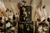 a sophisticated wedding cake in black, with gold leaf, sugar rocks and dried blooms on top is stylish for Halloween