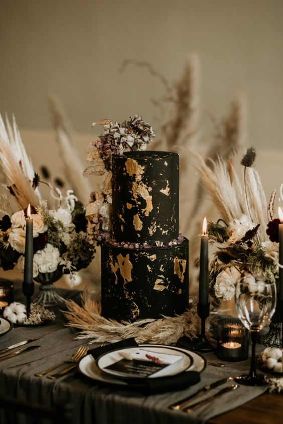 a sophisticated wedding cake in black, with gold leaf, sugar rocks and dried blooms on top is stylish for Halloween