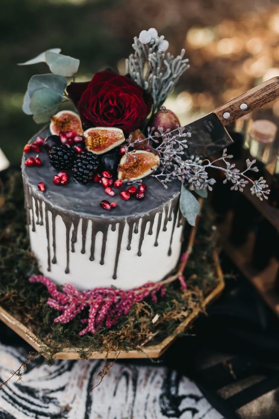 a stylish white wedding cake with grey drip, fresh berries, fruits and leaves and blooms is ultimate for Halloween