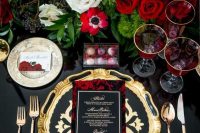 a very sophisticated and decadent wedding tablescape with gold chargers and cutlery, lush red roses and all black around
